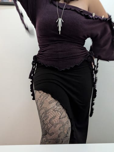 Vista parcial de una clienta usando el suéter/vestido "She Shell" color arándano, combinado con una falda negra.