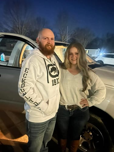Reviewer smiling outdoors at night while wearing the long, wavy Sensationnel Bare Lace Wig.