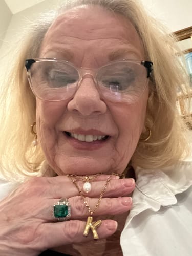 Close-up of a reviewer holding a gold Bubble Letter Initial Necklace with a 'K' pendant in her hand.