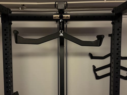 Kunde zeigt den breiten Ergo-Griff aus dem Set, der an einem schwarzen Latzugturm befestigt ist.