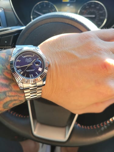 Customer's silver Lucky Fours® Spine watch with a blue dial, worn on a tattooed wrist inside a car.