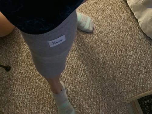 Reviewer wearing a grey knee sleeve on their leg while standing on a brown carpet.