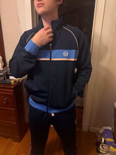 Customer wearing the Lago Track Pant in Maritime Blue with the matching track jacket indoors.