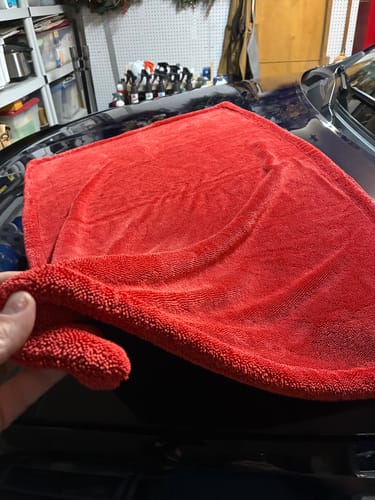Customer's hand holding a corner of the plush red BLACKLINEĀ® TWISTED-LOOP DRYING TOWEL on a car.
