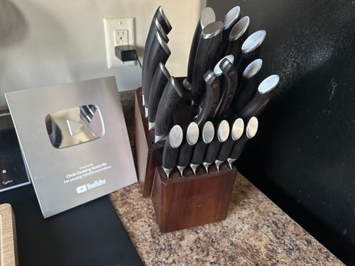Reviewer's Loong-21 Piece Chef Knife Set in its wood block on a kitchen counter, placed next to a YouTube Creator Award plaque.