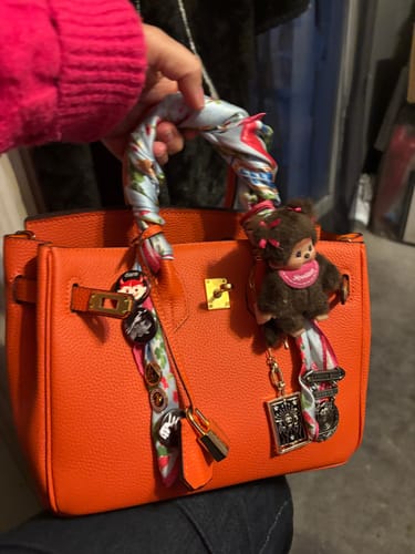 Customer holds their bright orange LALUVA Warkin Leather Bag, personalized with a scarf and charms.