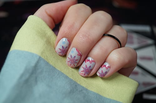 Die Hand eines Rezensenten zeigt die aufgetragenen 'Holiday Glitter And Glam' Nagelfolien mit einem festlichen rosa Schneeflocken-Design.