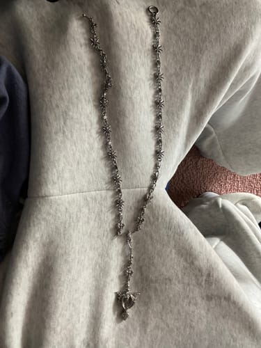 Reviewer's silver ROTTEN ROSARY necklace shown laid out on their grey hoodie.