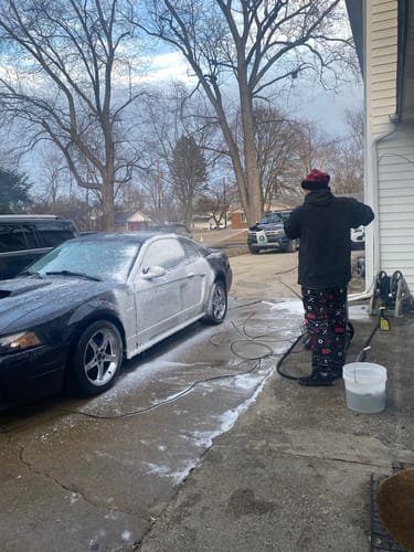 Customer's photo of a person spraying down a black car with thick foam in a driveway.