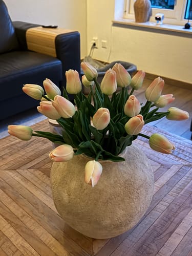 Klant toont het oudroze tulpenboeket in een grote vaas op een salontafel.