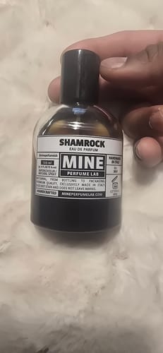 Recensore che tiene in mano la boccetta di profumo SHAMROCK dal liquido scuro.