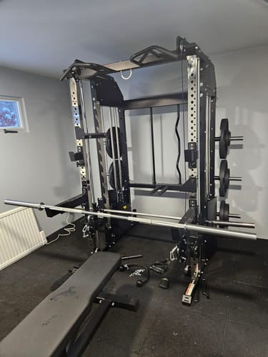Rezensent zeigt die gusseisernen Hantelscheiben aufbewahrt an einem schwarzen Power-Rack in einem Heimstudio.
