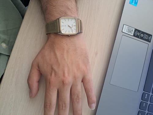 Reseñador mostrando su reloj Citizen Quartz dorado en la muñeca, junto a un portátil sobre una mesa.
