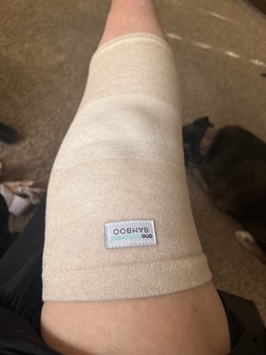 Customer wearing the beige Premium Bamboo Knee Sleeve, showing the fit on their leg indoors.