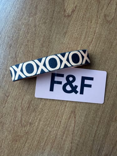 Customer's F&F Colorwheel Bracelet with a repeating dark XOXO pattern, shown next to its F&F card.