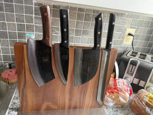 Reviewer's Walnut Magnetic Knives Holder on a kitchen counter, holding four large, dark knives.