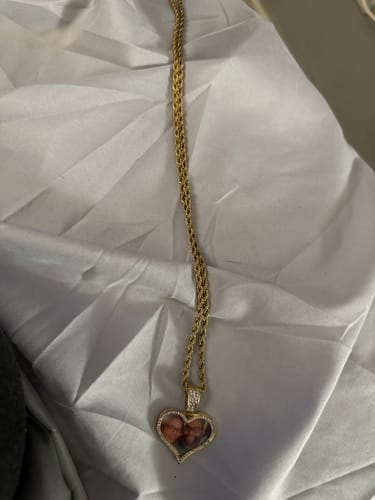 Customer's personalized heart-shaped photo necklace with a gold-colored chain, resting on a white cloth.
