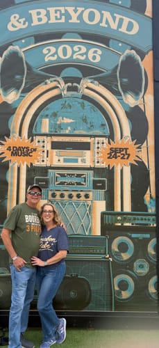 Reviewer standing in front of a festival sign, wearing a green Like Bourbon Maybe 3 People T-Shirt