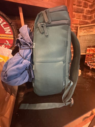 Customer's green The Organizer 20L backpack standing on a counter with a blue sweater strapped to the side.