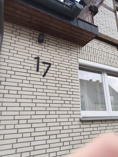 Kunden-Foto der modernen schwarzen Hausnummer 17 montiert an einer hellen Ziegelwand neben einem Fenster.