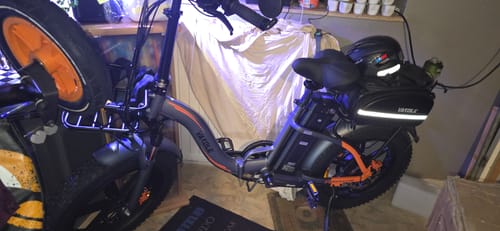 Reviewer's dark grey Vakole Y20 Pro e-bike parked indoors with a black seat bag, helmet, and front basket attached.