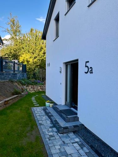 Customer's moderne Hausnummer 5a als schwarzes Wandschild an der weißen Fassade eines Hauses montiert.
