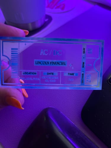 Customer's personalized acrylic concert ticket ornament for AC/DC held in a hand against a purple-lit background.