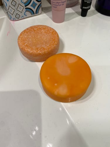 Customer's two round Jasmine Shine & Volume Conditioner and shampoo bars resting on a white bathroom counter.
