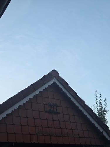 Kunden-Hausnummer montiert an der Giebelspitze eines Ziegeldachs vor einem klaren blauen Himmel.