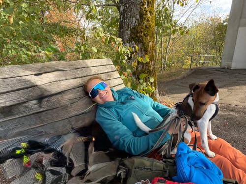 Kundens turkise Allround Zip Shirt med hund på skødet, mens de slapper af på en træbænk i skovklædte omgivelser.