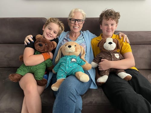 Reviewer en twee kinderen zittend op een bank, elk vasthoudend aan hun eigen Hond Kleding Origineel Lotgenootje knuffel.