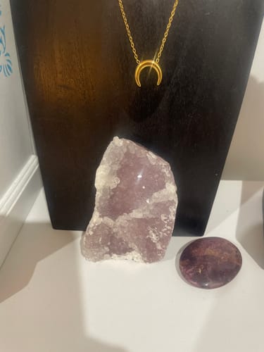 Customer's Traveler crystals and a gold-toned crescent necklace displayed on a black stand.