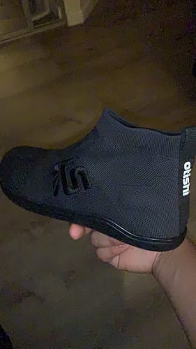 Customer's black Otishi 2.0 Amaru Black shoe held in hand, highlighting the knit upper and side branding.