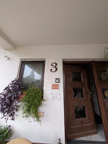Kundenfoto der geschwungenen WesterWerk-Hausnummer '3' in dunkler Optik, montiert an einer hellen Hauswand.