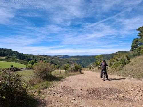 Reviewer riding their Lankeleisi e-bike on a gravel path in a sunny, mountainous landscape.