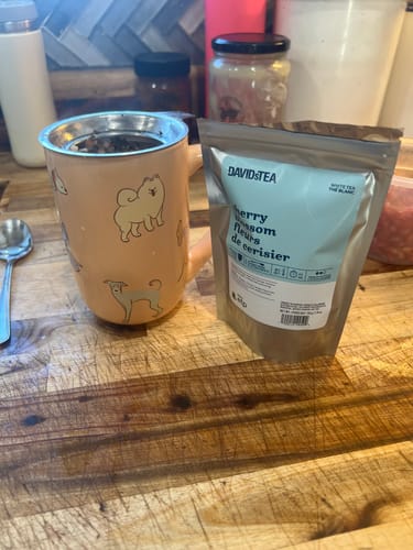 Customer's Cherry Blossom tea pouch next to a tan dog-themed mug on a wooden surface.