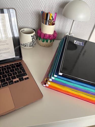 Customer's stack of multicolored Oxford European Book spiral notebooks on a desk next to a laptop.