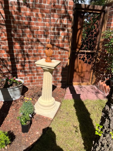 Customer's Colonel Barkley dog bust in rust-colored iron, displayed on a pedestal in a brick garden setting.