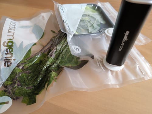 Customer's Vacuum Genie sealing herbs in clear vacuum bags on a wooden surface.