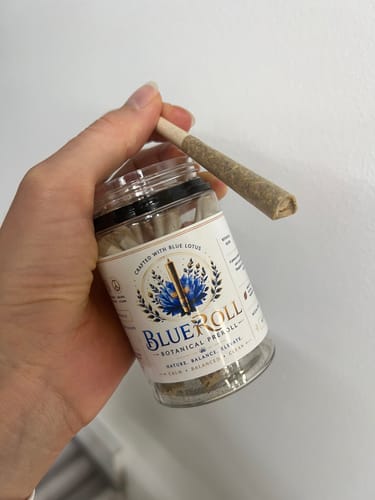 Customer's hand holding a BlueRoll botanical pre-roll jar and a single pre-roll resting on top.