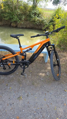 Customer's orange and black Lankeleisi MG600 Pro e-mountain bike parked outdoors next to a small canal.