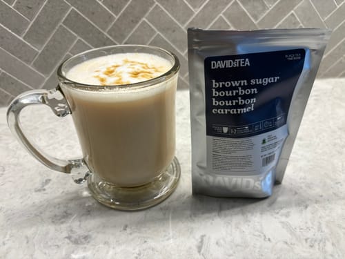 Reviewer's Brown Sugar Bourbon tea prepared as a creamy latte next to the tea package on a marble counter.