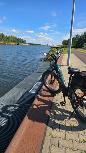 Customer's Lankeleisi MG600 Plus fat bike parked on a paved waterfront path next to a canal under a clear blue sky.