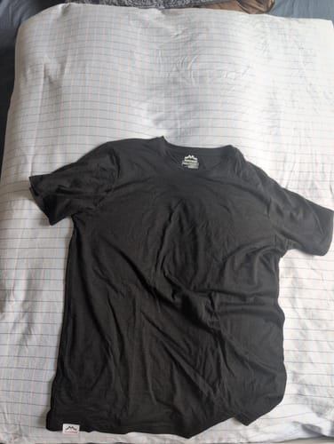 Customer's schwarzes Merino Shirt Herren auf einem hellen Bettlaken ausgebreitet.