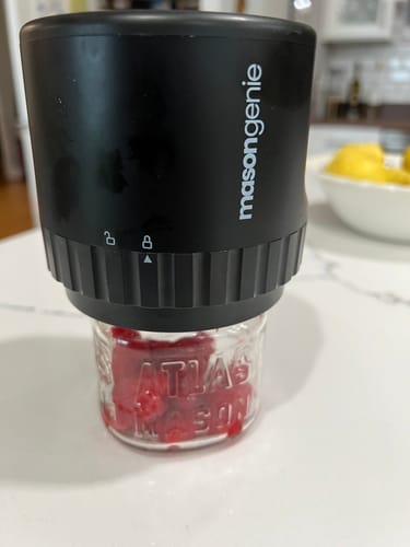 Customer's black Mason Genie vacuum sealer active on a glass jar filled with raspberries on a kitchen counter.