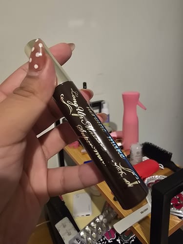 Customer's hand holding a brown Kiss Me Heroine Long UP Mascara tube against a blurry background.