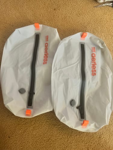 Customer's two white Aerless Luggage Tags featuring black zippers and orange accents laying on a carpet.