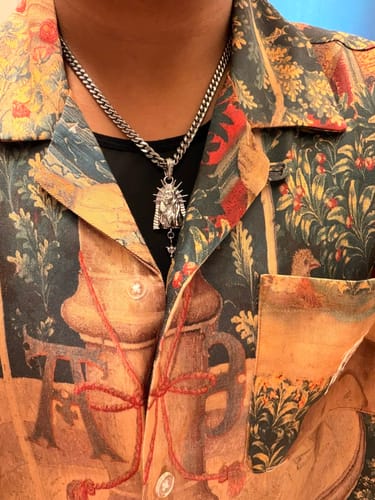 Customer's silver Virgin Mary pendant worn on a chain against a patterned shirt.