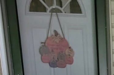 Customer's personalized pumpkin-shaped door hanger displayed on a white front door.