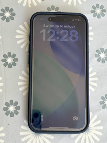 Customer's Apple iPhone 15 Pro in a blue case on a floral surface, displaying the lock screen.